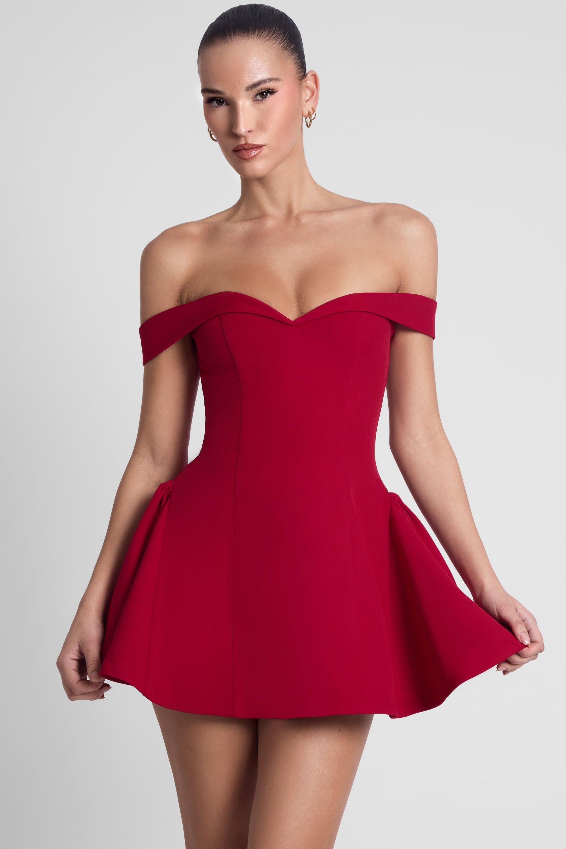 Burgundy sweetheart off shoulder corset mini dress with flared skirt, hands holding hem detail