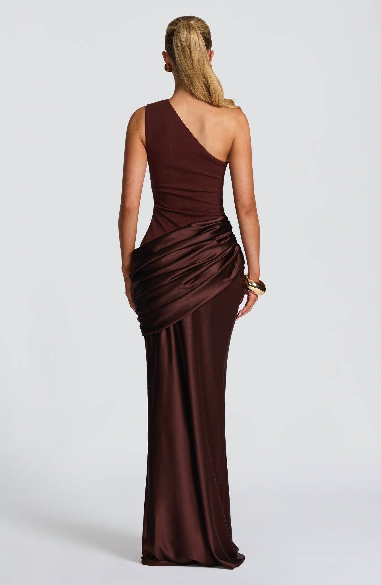 Back view of a women's chocolate brown one-shoulder draped formal maxi dress, highlighting the elegant silhouette and draped detail.