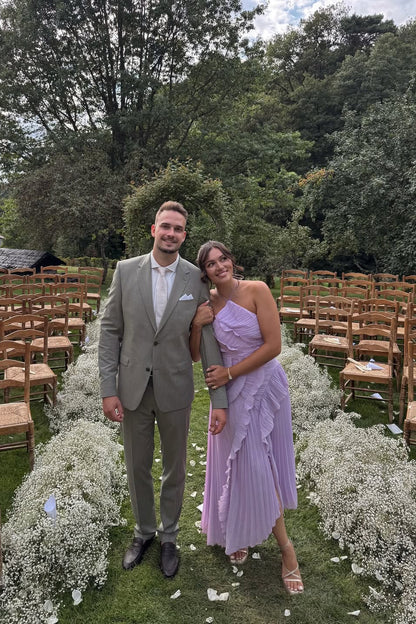 Couple posing, woman in a pink one-shoulder ruffle pleated midi dress, man in a tailored grey suit.