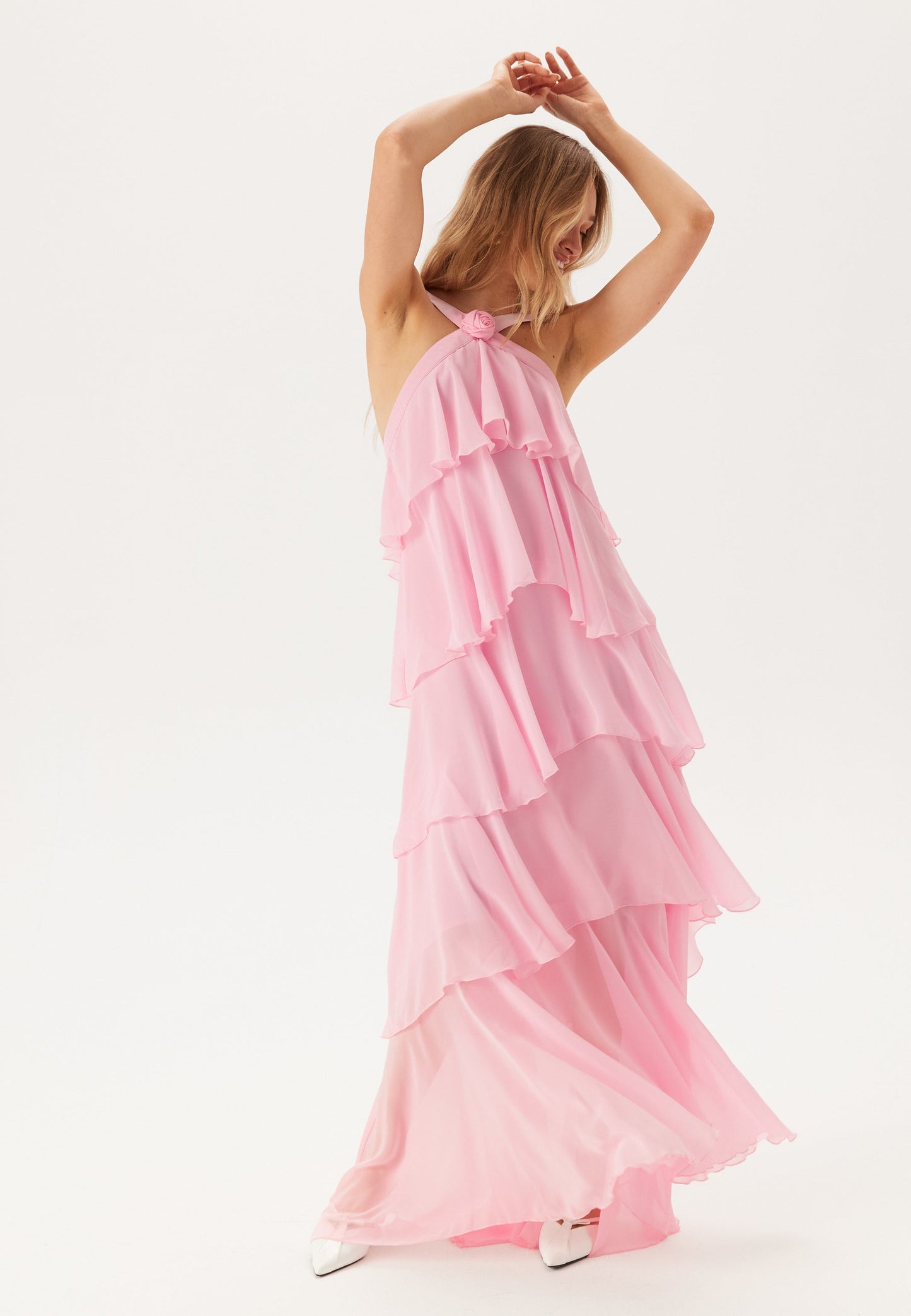 Full body shot of a woman posing in a flowing pink tiered ruffle maxi dress, ideal as a vacation dress or for wedding guests.