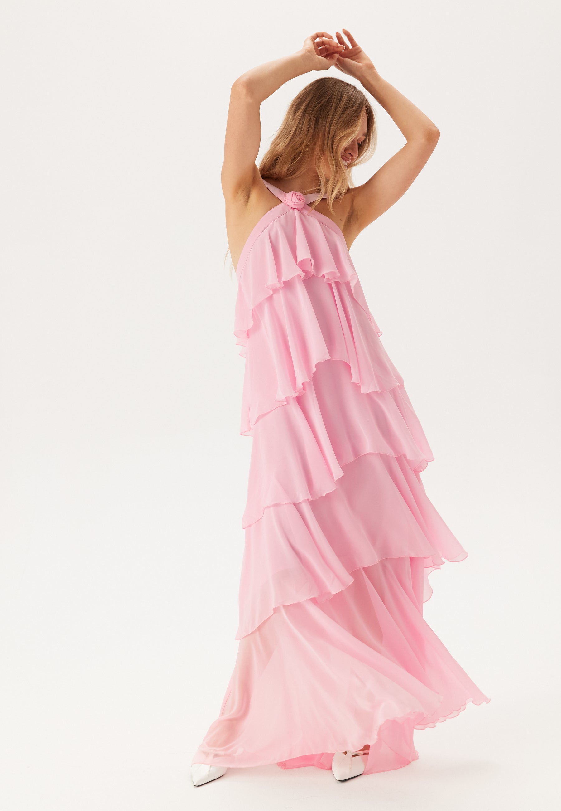 Full body shot of a woman posing in a flowing pink tiered ruffle maxi dress, ideal as a vacation dress or for wedding guests.