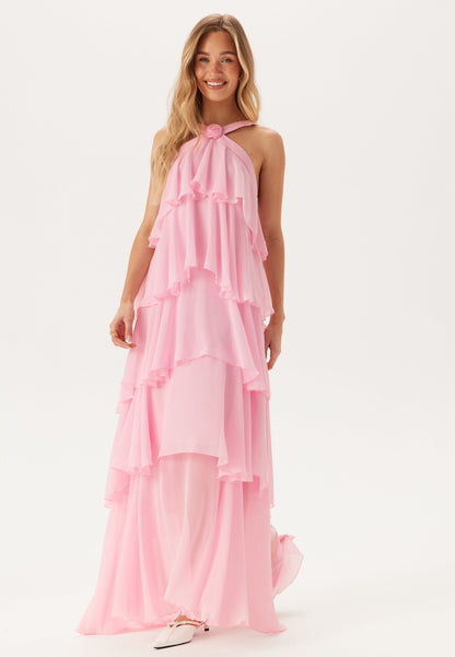 Front view of a blonde woman wearing a pink tiered ruffle maxi dress with a halter neck and small rose detail.