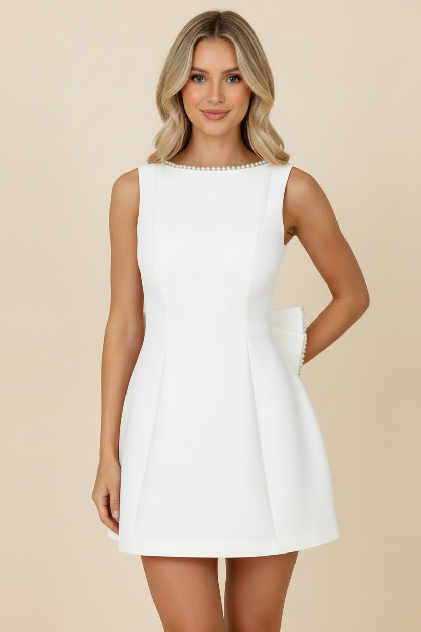 Front view of a white sleeveless mini dress with a pearl-trimmed neckline and a hint of the large bow on the back.