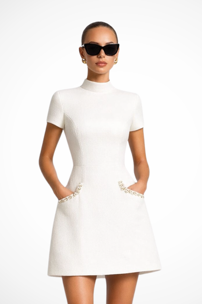 White pearl trim mock neck mini dress with short sleeves and decorative front pockets, front view.