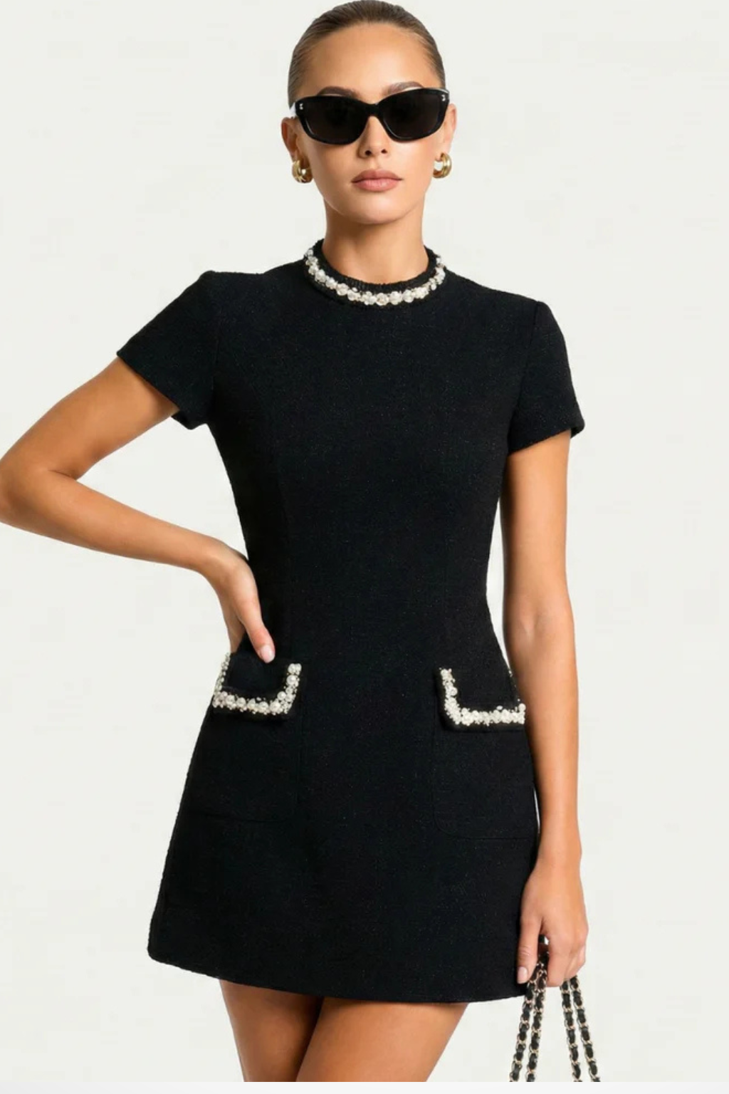 Black pearl trim mock neck mini dress with short sleeves and pearl-edged pockets, side pose.