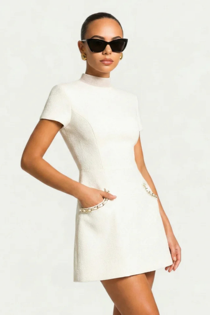 Side view of white pearl trim mock neck mini dress with short sleeves and chain-pearl pockets.