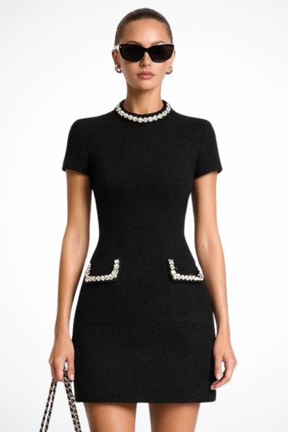 Black pearl trim mock neck mini dress with short sleeves and front pockets, styled with sunglasses.