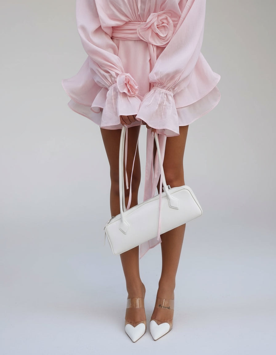 Close-up of the light pink long sleeve mini dress showing the rosette tie, ruffled cuffs, and layered skirt detail.