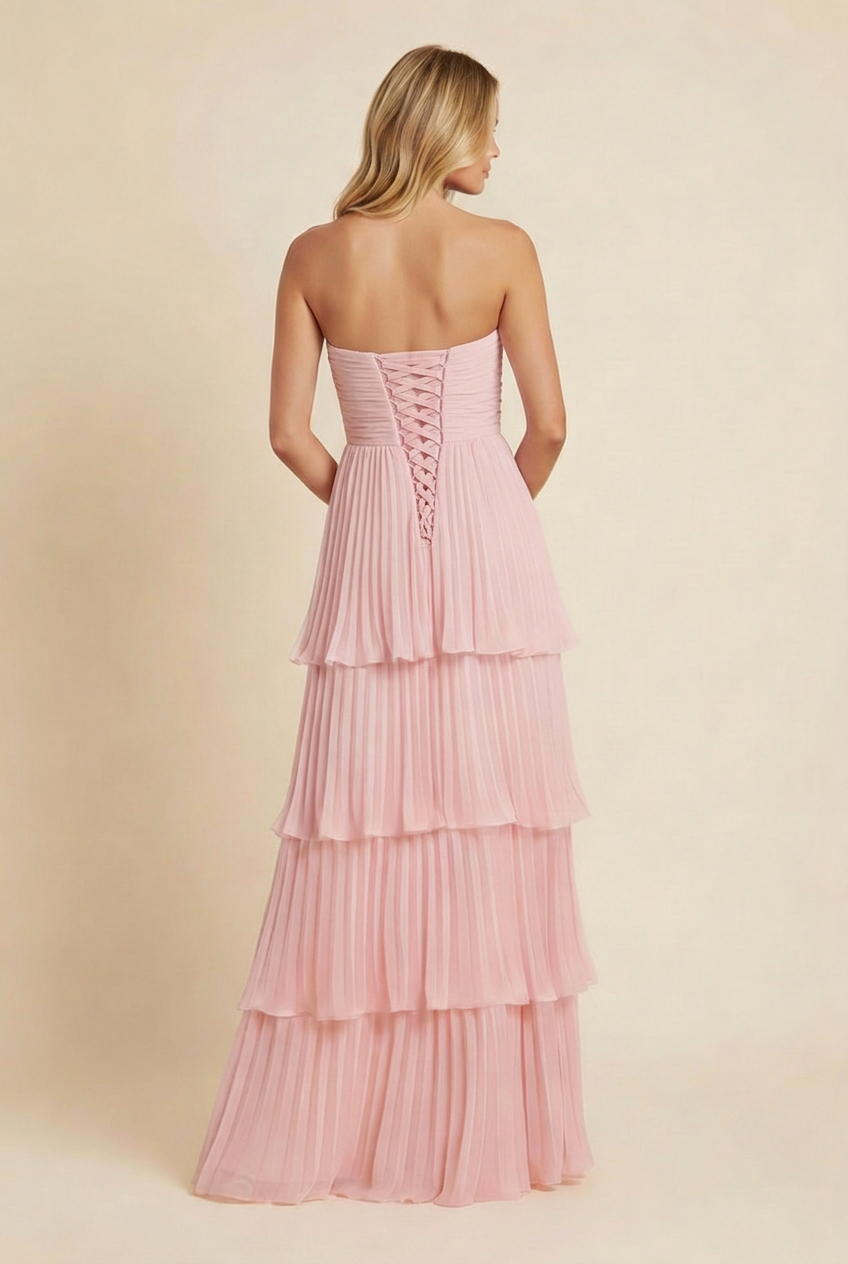 Back view of a light pink strapless tiered maxi dress featuring a lace-up corset detail and flowing pleated skirt