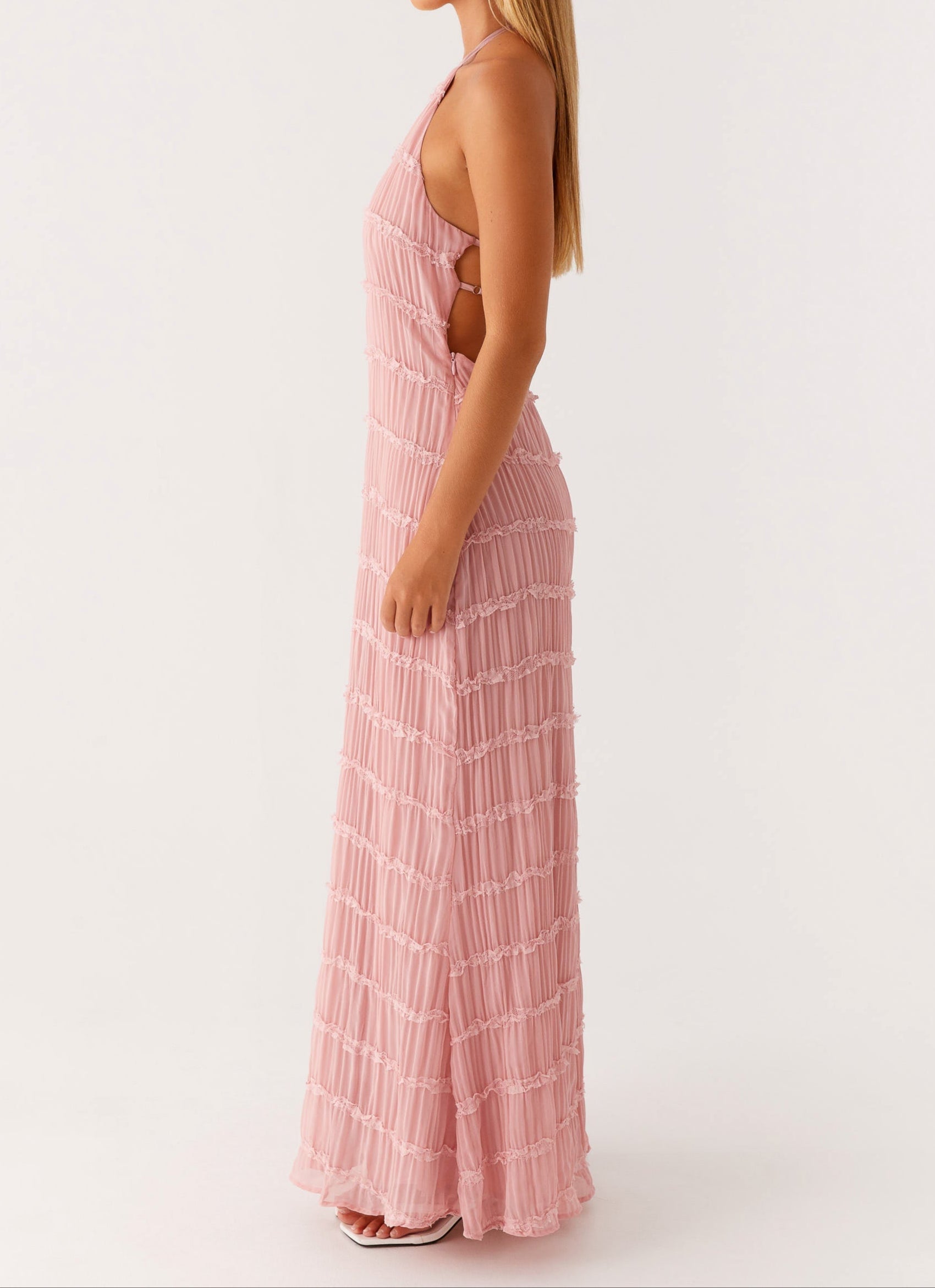 Side view of blush pink halter maxi dress showing open sides, pleats, and ruffle hem