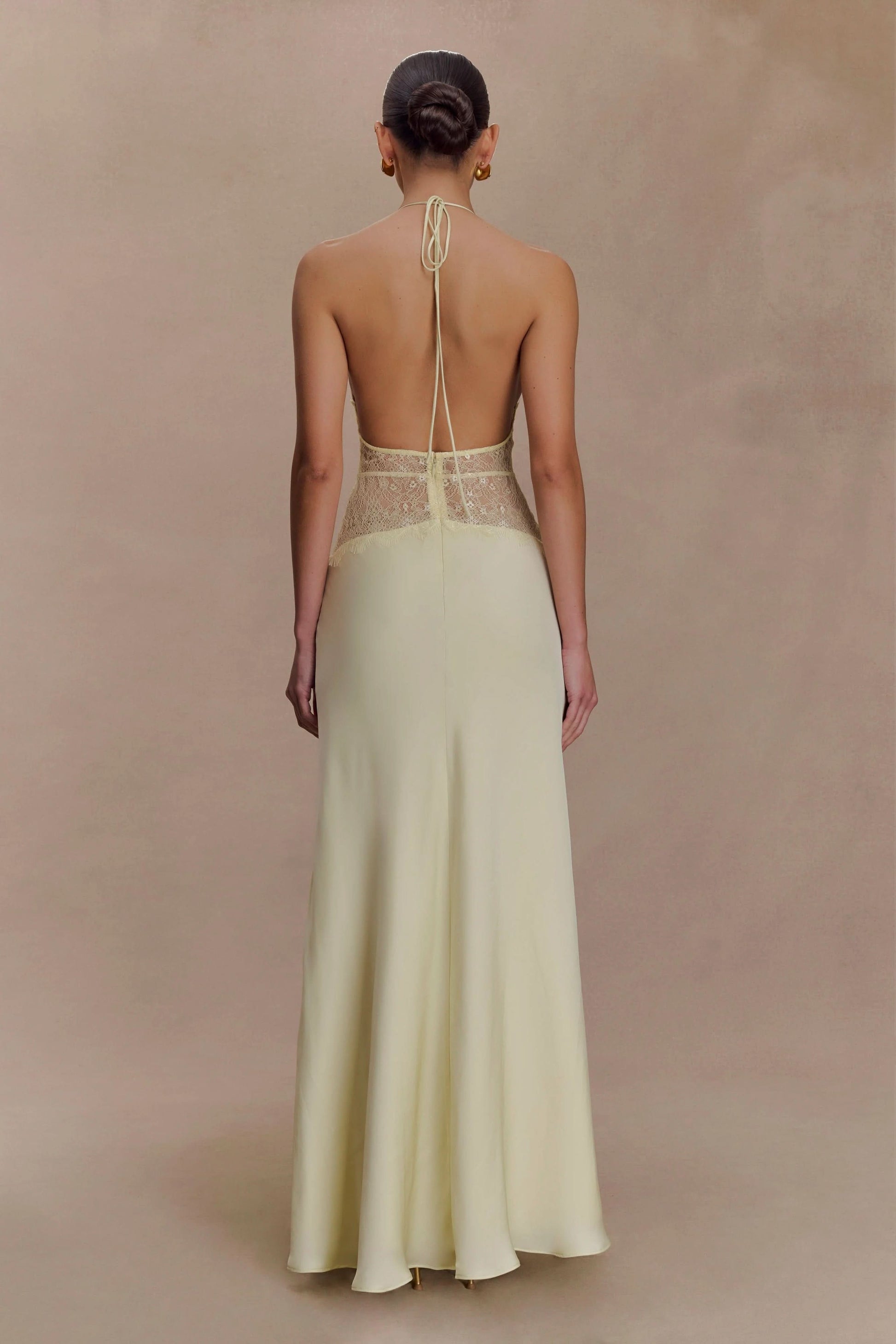 Back view of a women's pale yellow halter V-neck maxi dress, showcasing the open back and lace details, an elegant dress for wedding guests.