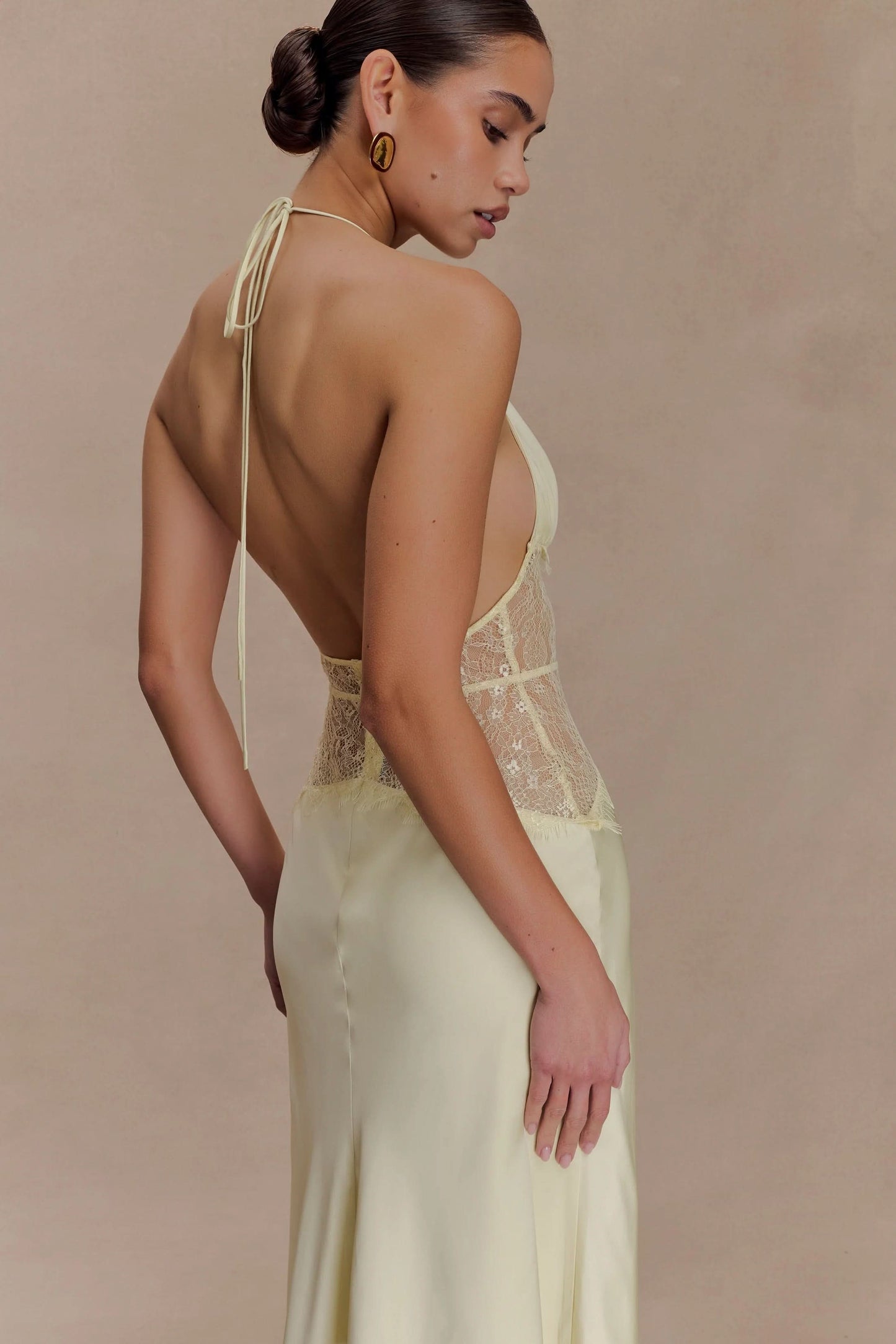 Side profile of a women's pale yellow halter V-neck maxi dress, highlighting the intricate lace bodice and flowing skirt.
