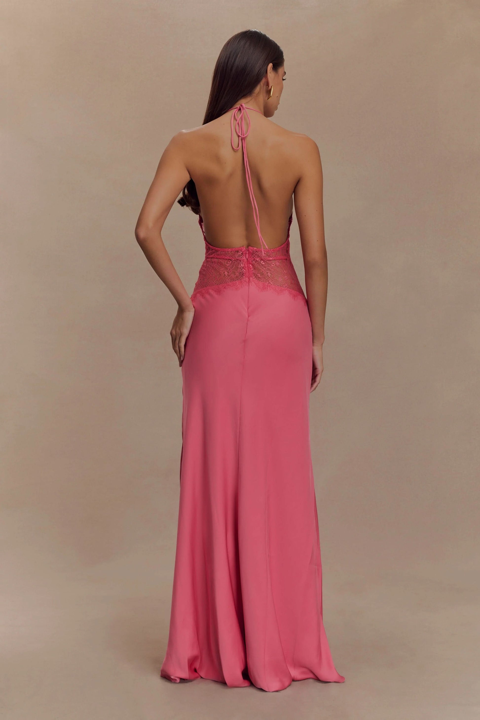 Back view of a women's vibrant pink halter V-neck maxi dress, featuring an open back design and lace accents, a beautiful elegant dress.