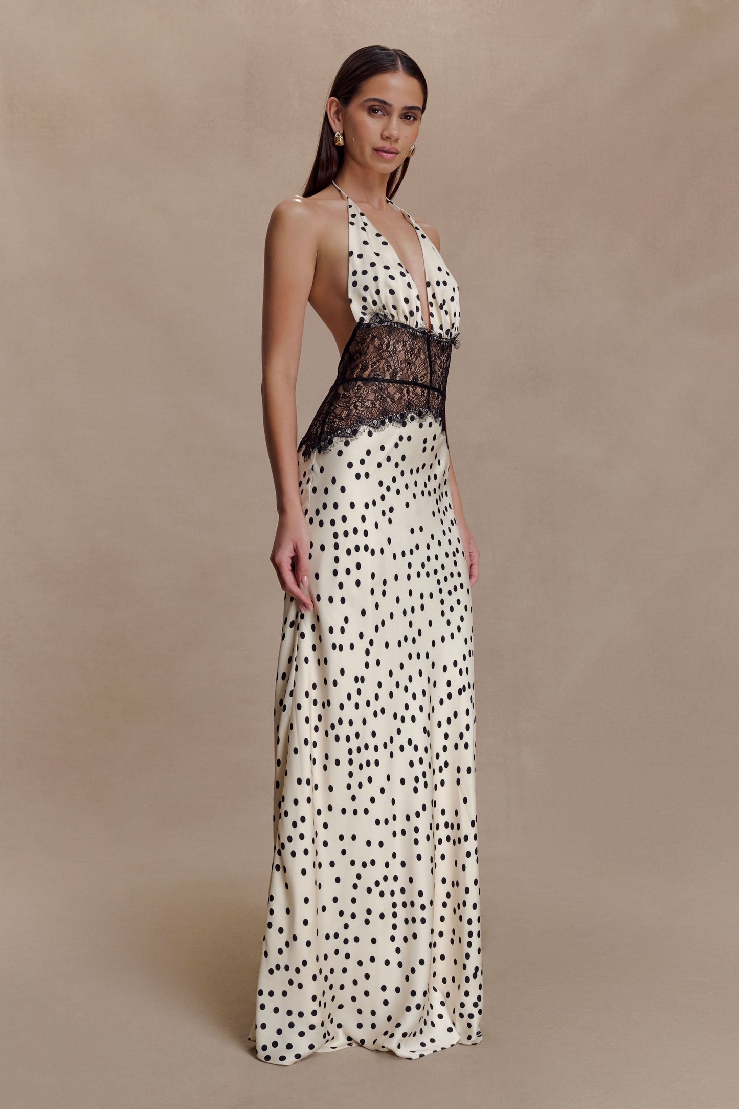 Side view of a women's cream polka dot halter V neck maxi dress with black lace bodice, showing flowy skirt.