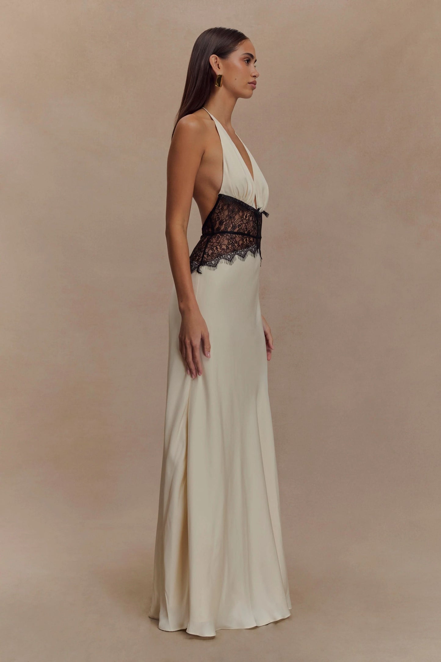 Side view of a women's cream halter V neck maxi dress, highlighting the black lace bodice and long skirt.