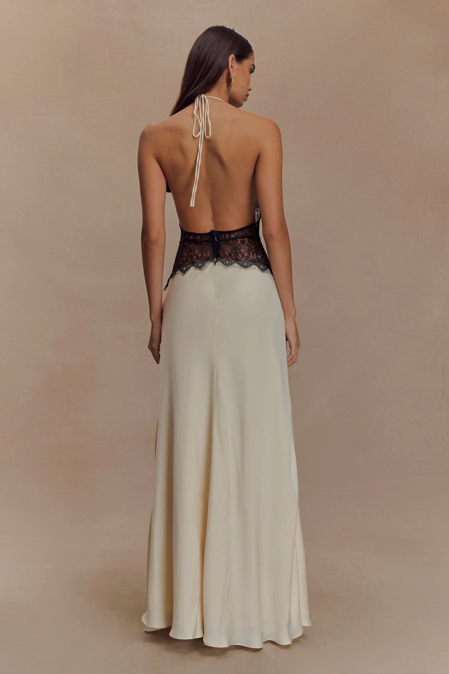 Back view of a women's cream halter V neck maxi dress with black lace bodice and an open back, perfect for wedding guests.