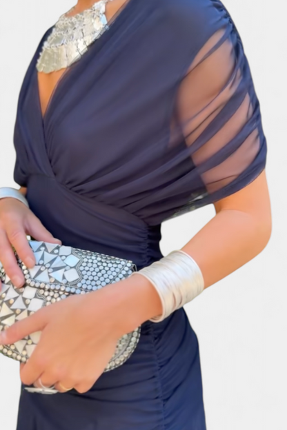 Navy blue ruched maxi dress with draped neckline and sheer sleeve overlay, side close-up view