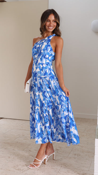 Side view of a woman wearing a blue and white printed one-shoulder midi dress, posing with a white clutch and white strappy heels.