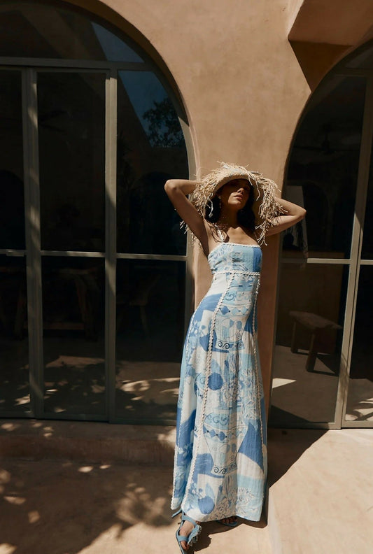 Women's blue and white printed maxi dress with ric rac trim and tie back, styled with a straw hat, perfect for vacation outfits.
