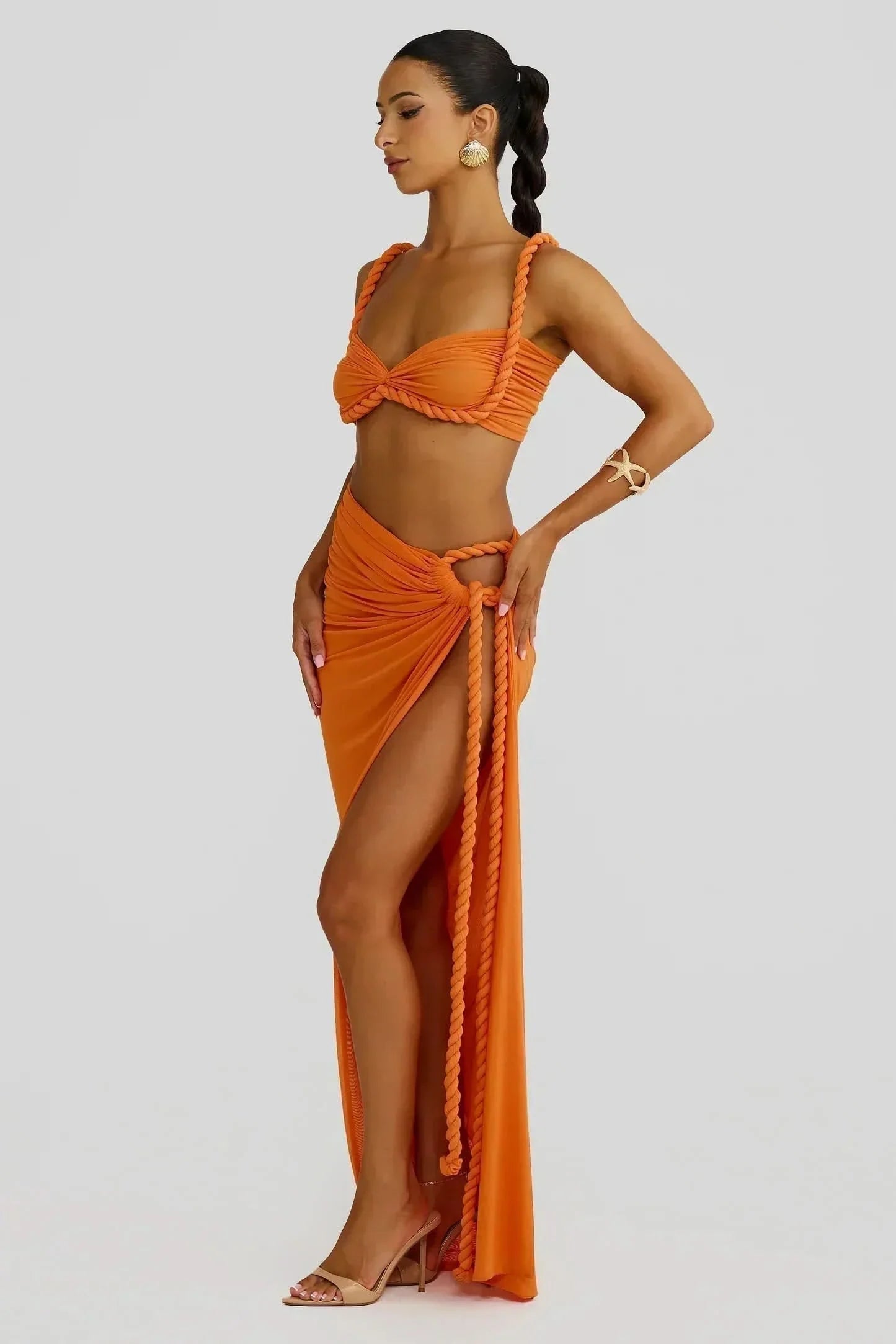 Side view of a women's orange ruched cut out maxi 2 piece set, highlighting the high slit and braided rope.