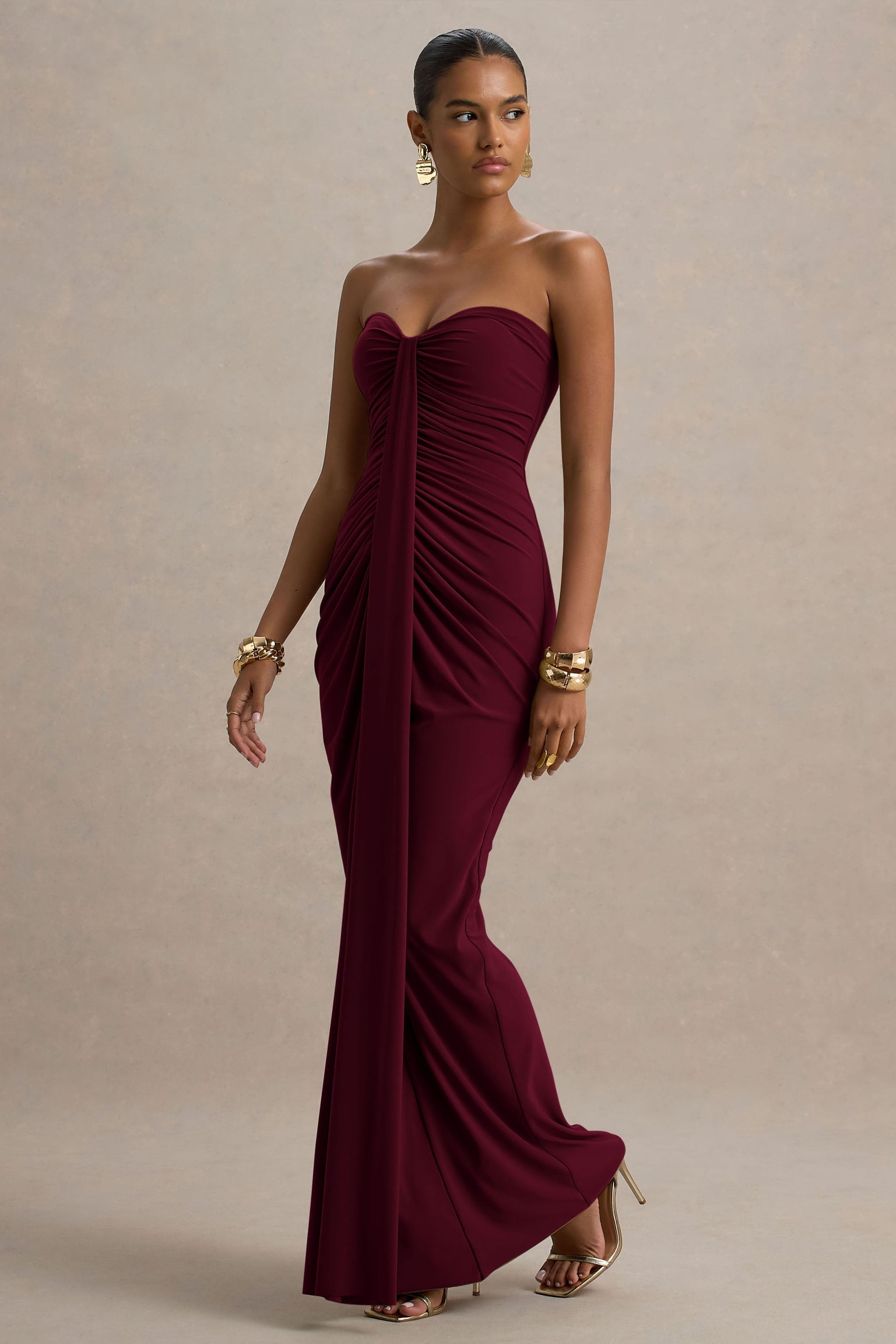 Angled view burgundy off shoulder ruched maxi dress in slinky jersey with draped front panel and long hem