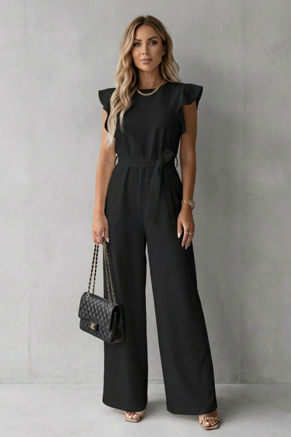 Full body shot of a women's black ruffle sleeve wide leg jumpsuit, featuring a tied waist belt.