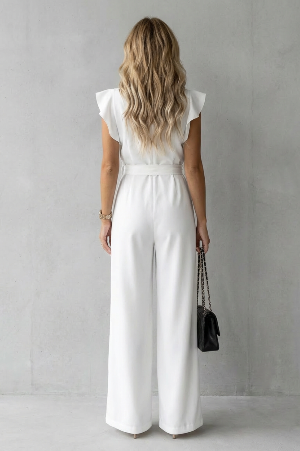 Back view of a white ruffle sleeve wide leg jumpsuit with a self-tie belt detail.