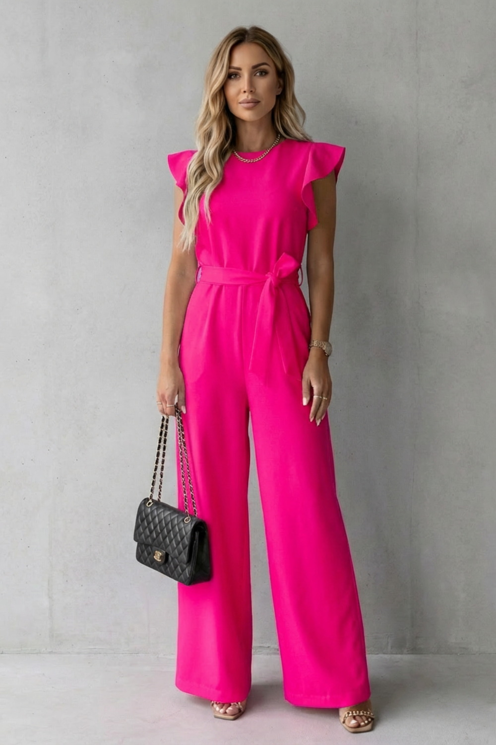 Full length front view of a fuchsia ruffle sleeve wide leg jumpsuit with a tied waist belt.
