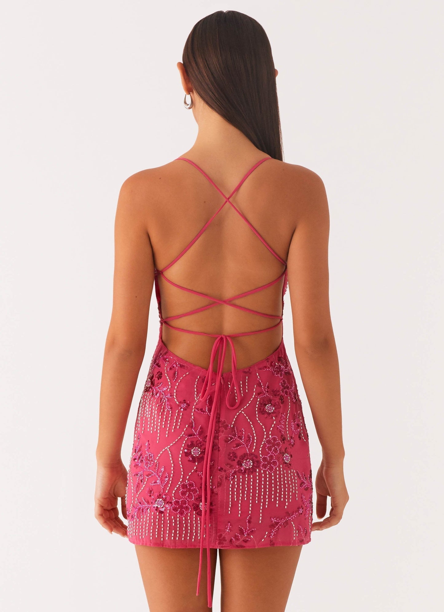 Back view of a fuchsia sequin mini party dress, featuring criss-cross back straps and a tie-up detail.