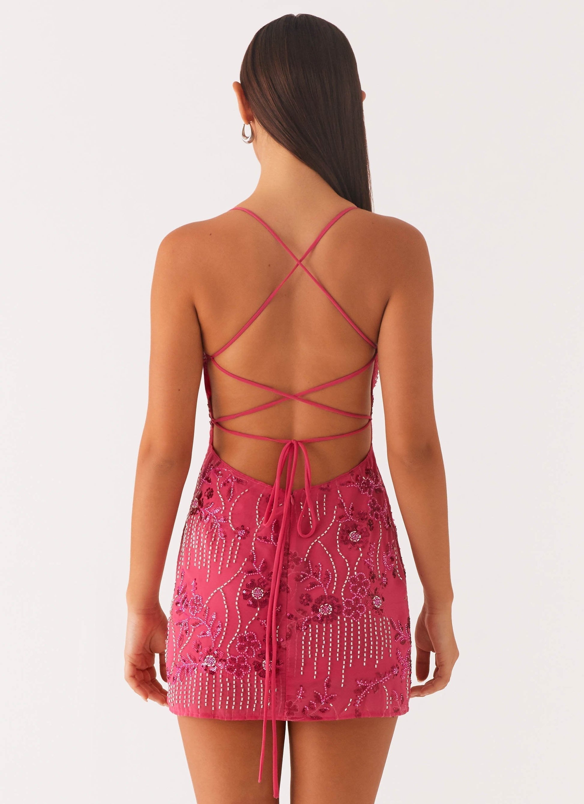 Back view of a fuchsia sequin mini party dress, featuring criss-cross back straps and a tie-up detail.