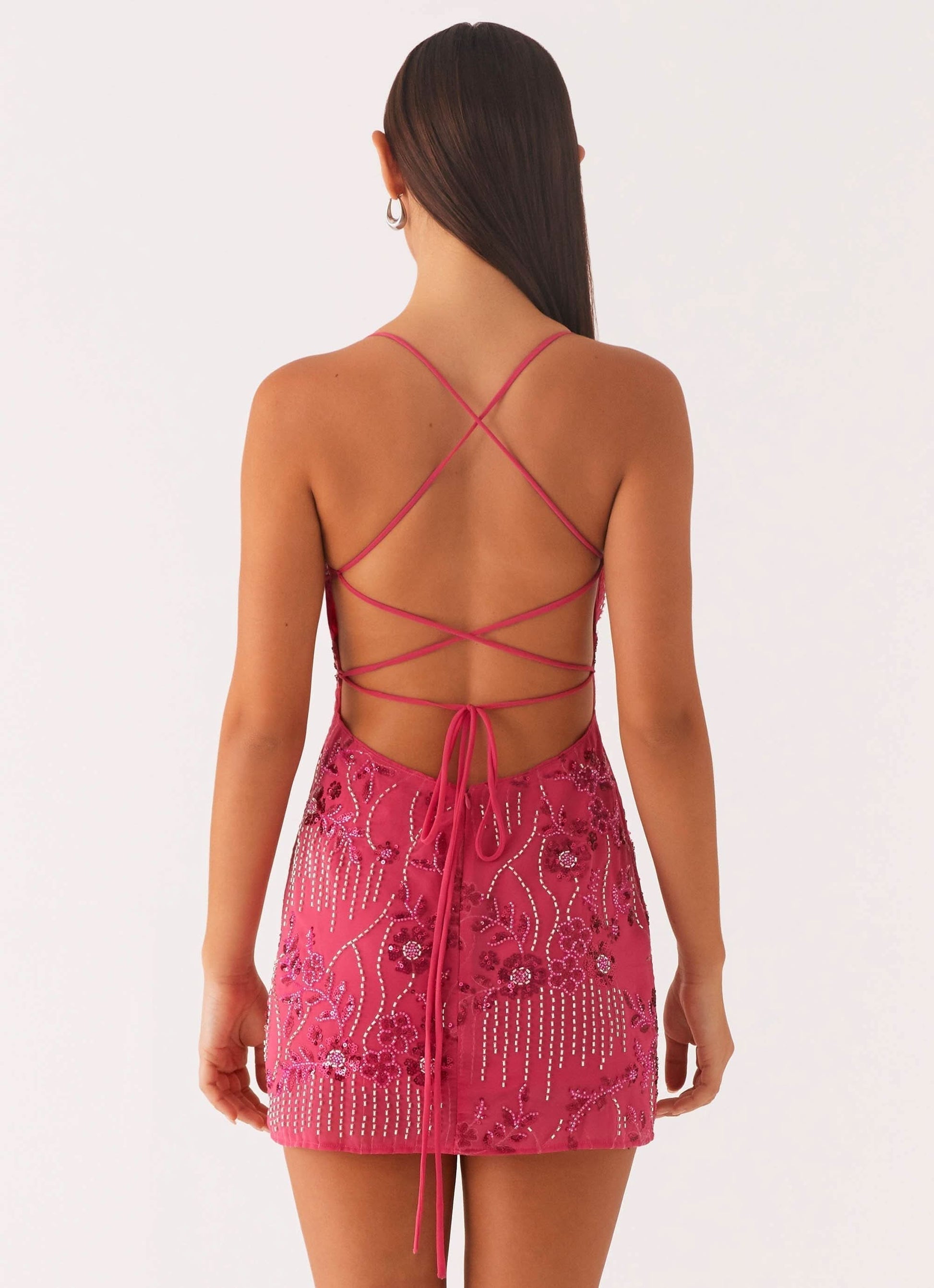 Back view of a women's fuchsia sequin mini dress, highlighting the elegant strappy open back design and beaded patterns.