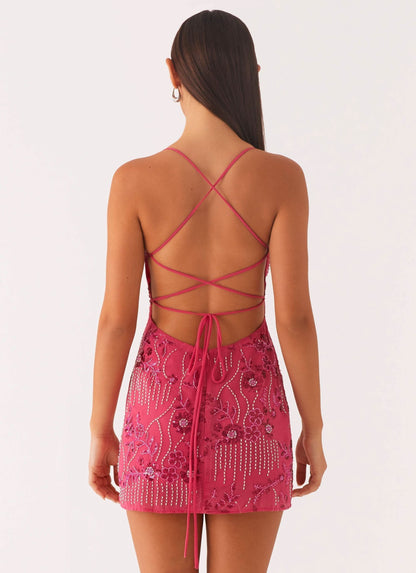 Back view of a women's fuchsia sequin mini dress, highlighting the elegant strappy open back design and beaded patterns.