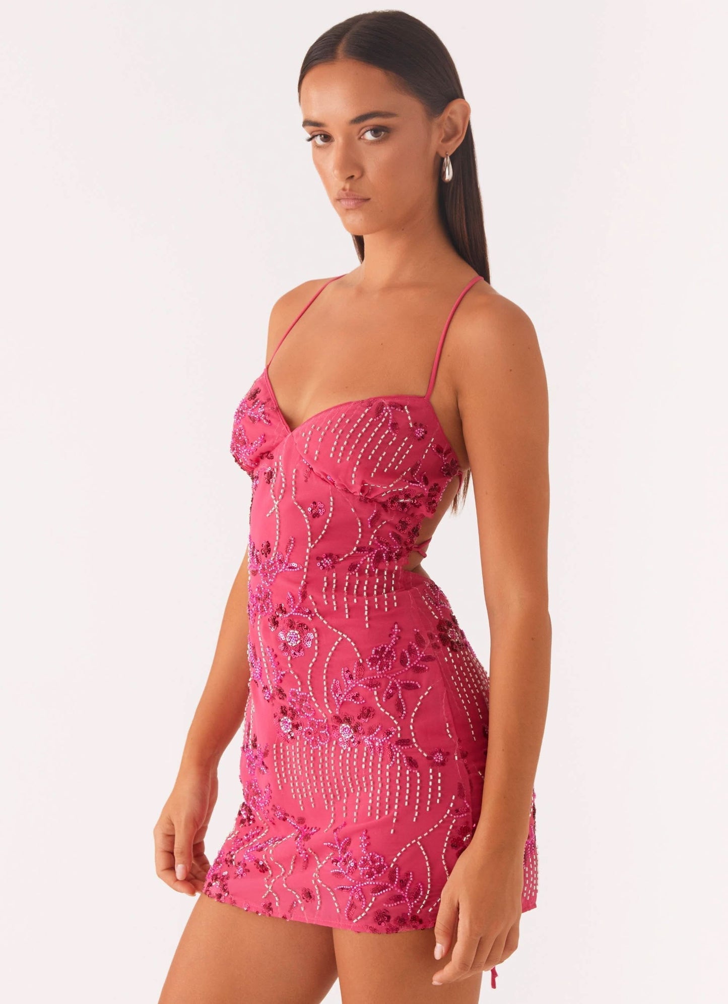 Angled front view of a women's fuchsia sequin mini dress, featuring the sweetheart neckline, floral beading, and side cut-out.