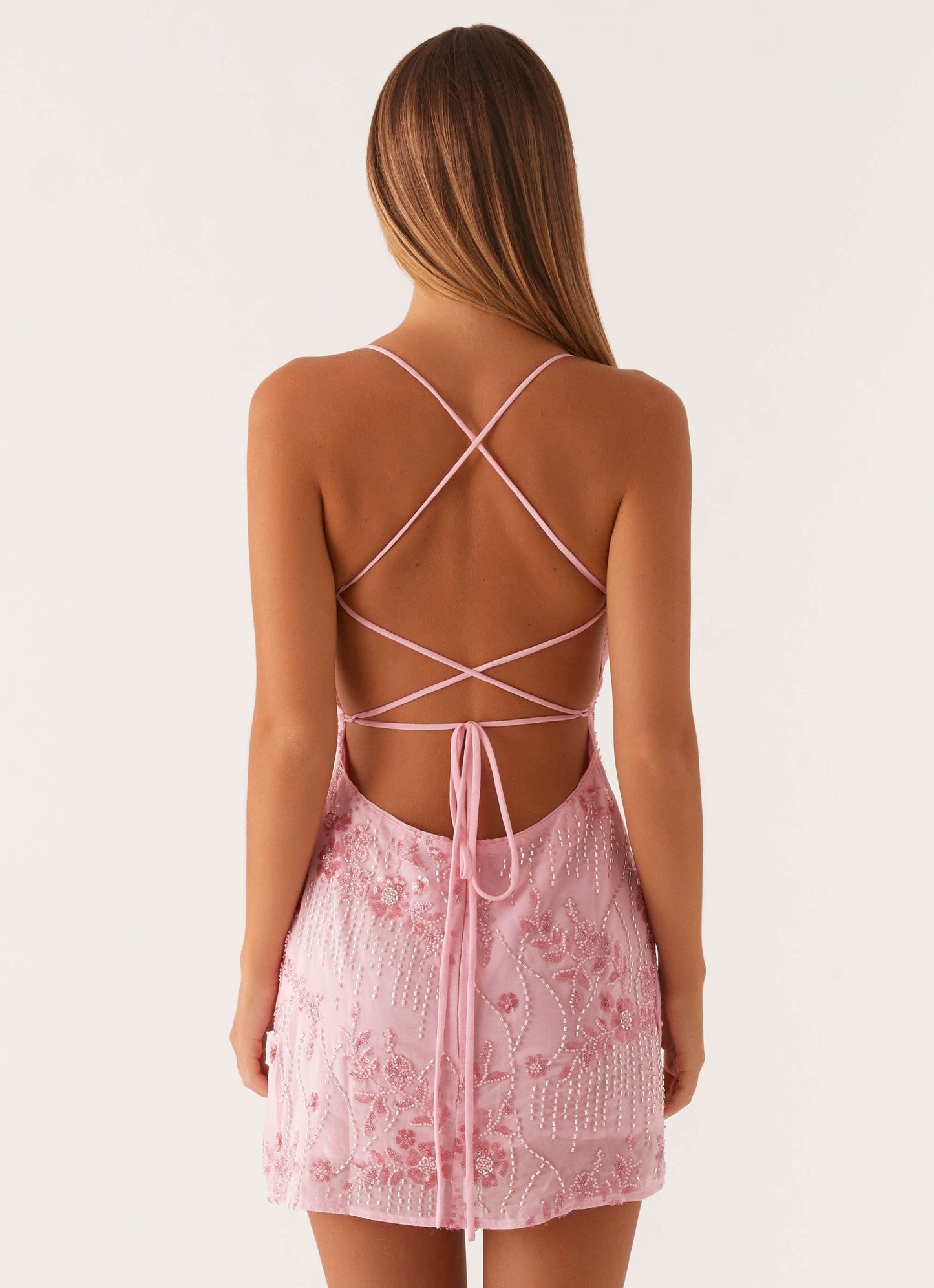 Back view of a women's pale pink sequin mini dress, displaying the intricate strappy open back and beaded floral patterns.