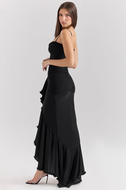 Side profile of a woman wearing a black sleeveless ruched ruffle high-low maxi dress, featuring a dramatic ruffled hem.