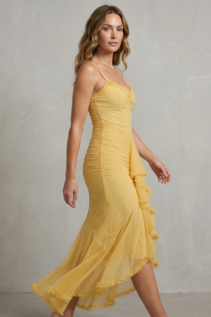 Side profile of a woman in a yellow sleeveless ruched ruffle maxi dress, highlighting the draped ruching and high-low hem with ruffles.