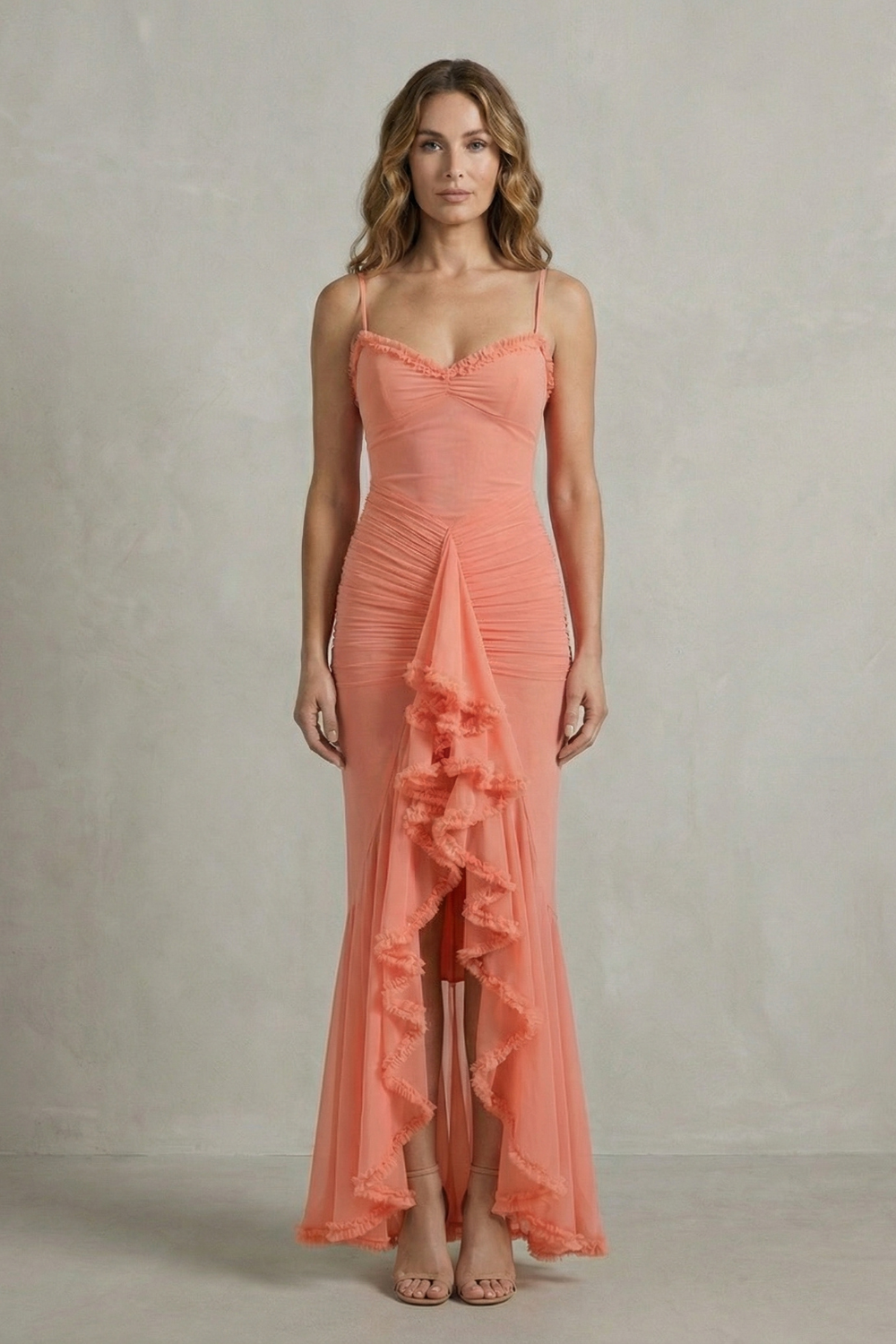Full-length front view of a woman wearing a coral sleeveless ruched ruffle maxi dress, ideal as a midi wedding guest dress.