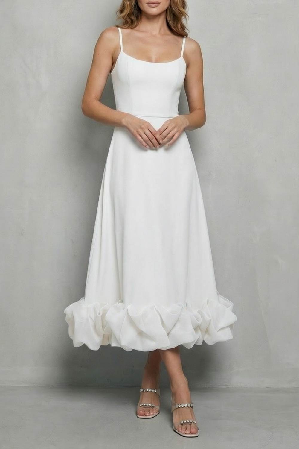 White sleeveless midi dress with thin straps and a voluminous ruffled hem, suitable as a white satin dress or elegant dress for wedding guests.