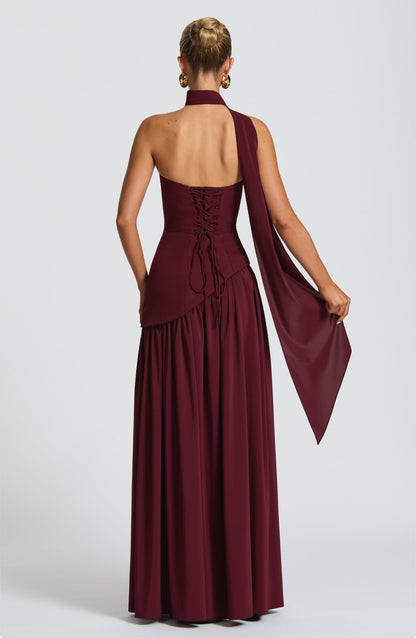 Back view of a women's strapless asymmetric corset maxi dress in burgundy, featuring a lace-up corset back and flowing scarf.