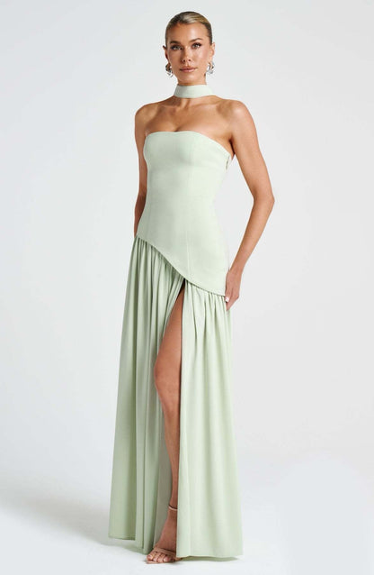 Full-length front view of a women's strapless asymmetric corset maxi dress in light sage green, highlighting the choker and high leg slit.