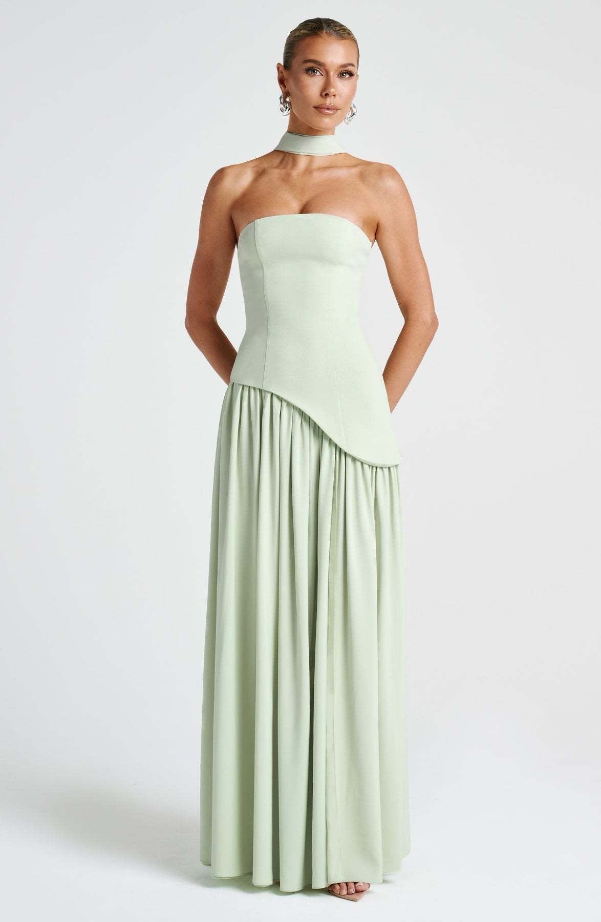 Front view of a women's strapless asymmetric corset maxi dress in light sage green, featuring a subtle asymmetric hem and choker neckline.