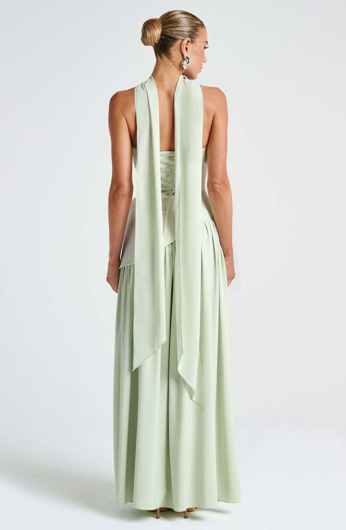 Back view of the light green strapless asymmetric corset maxi dress, featuring a lace-up corset detail and flowing fabric.