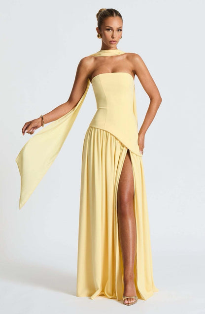 Full-length view of a model wearing the yellow strapless asymmetric corset maxi dress with a high leg slit and flowing panel.