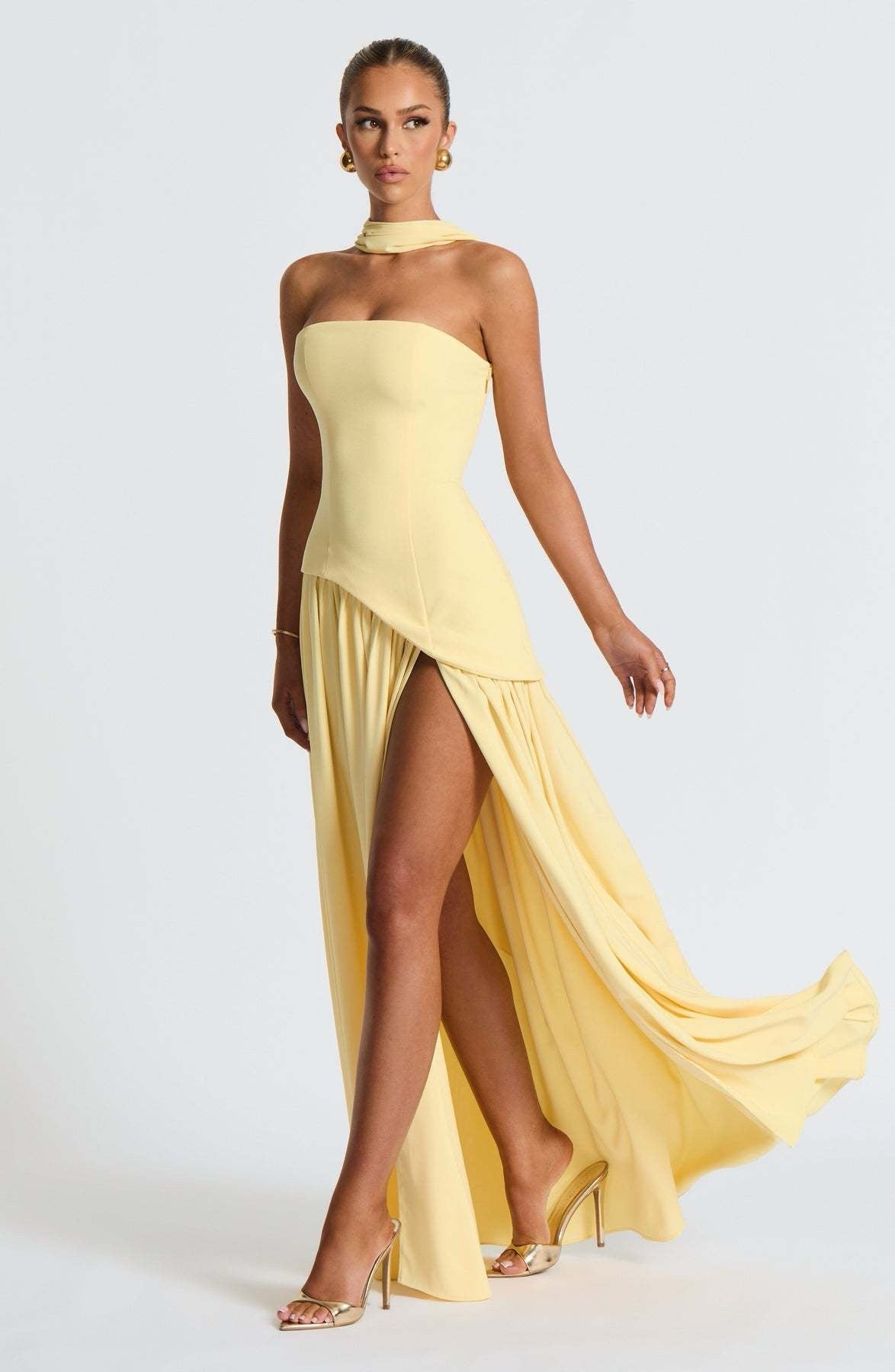 Dynamic shot of the yellow strapless asymmetric corset maxi dress with the skirt flowing, emphasizing the high leg slit.