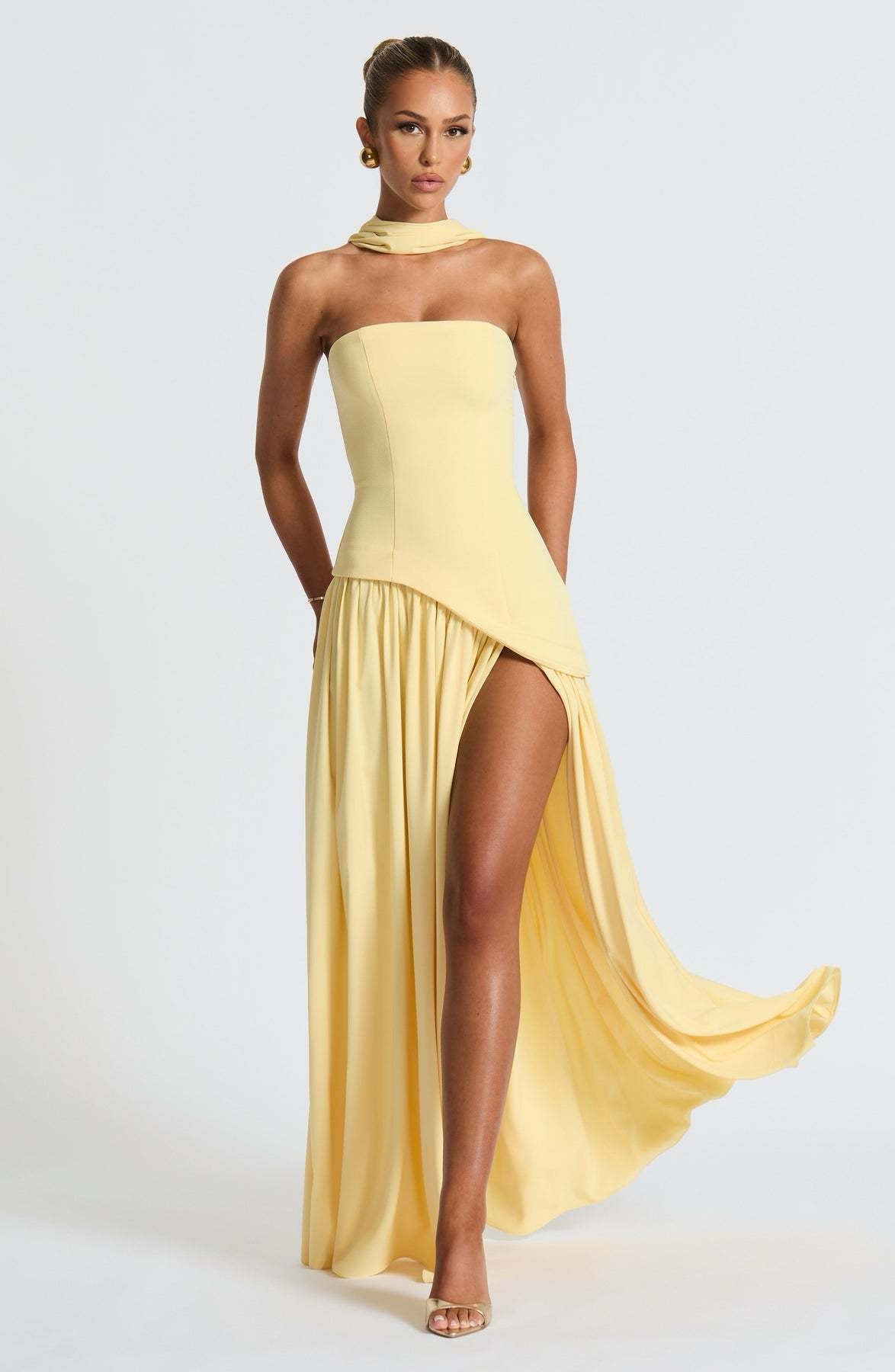 Front view of the yellow strapless asymmetric corset maxi dress, with the model's leg visible through the high slit.
