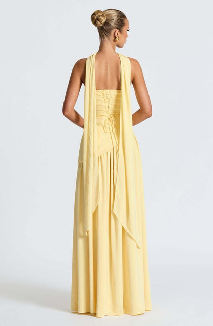 Rear view of the yellow strapless asymmetric corset maxi dress, showing the lace-up back and long, flowing ties.