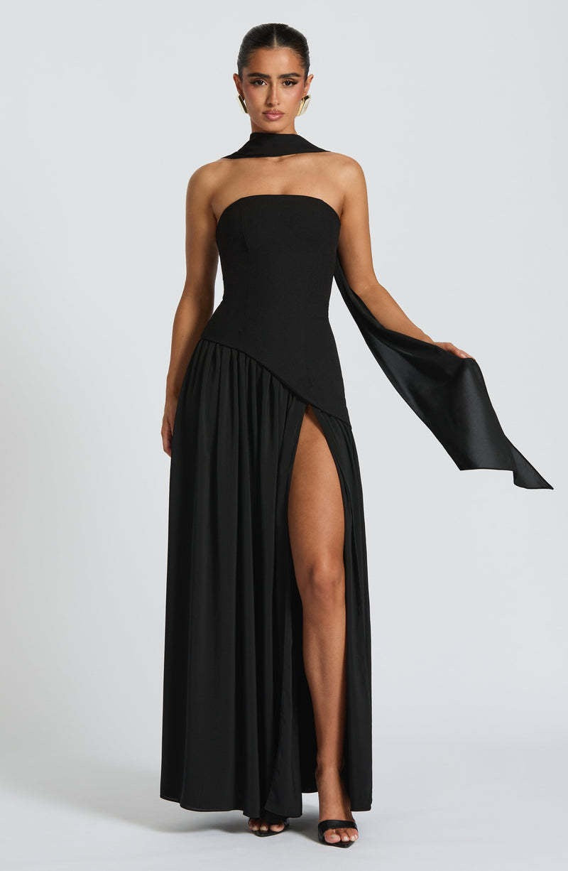 Model wearing a black strapless asymmetric corset maxi dress, with a high leg slit and dramatic flowing panel.