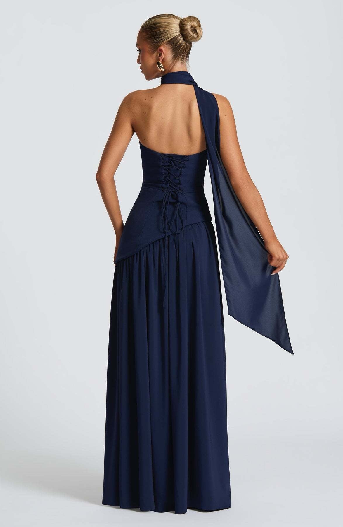 Back view of a navy blue strapless maxi dress showing the lace-up corset detail and a long flowing scarf.