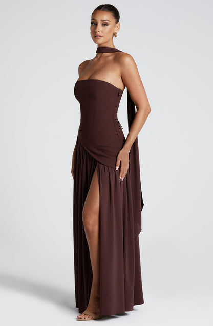 Profile view of a brown strapless asymmetric corset maxi dress, highlighting the flowing skirt and side slit.