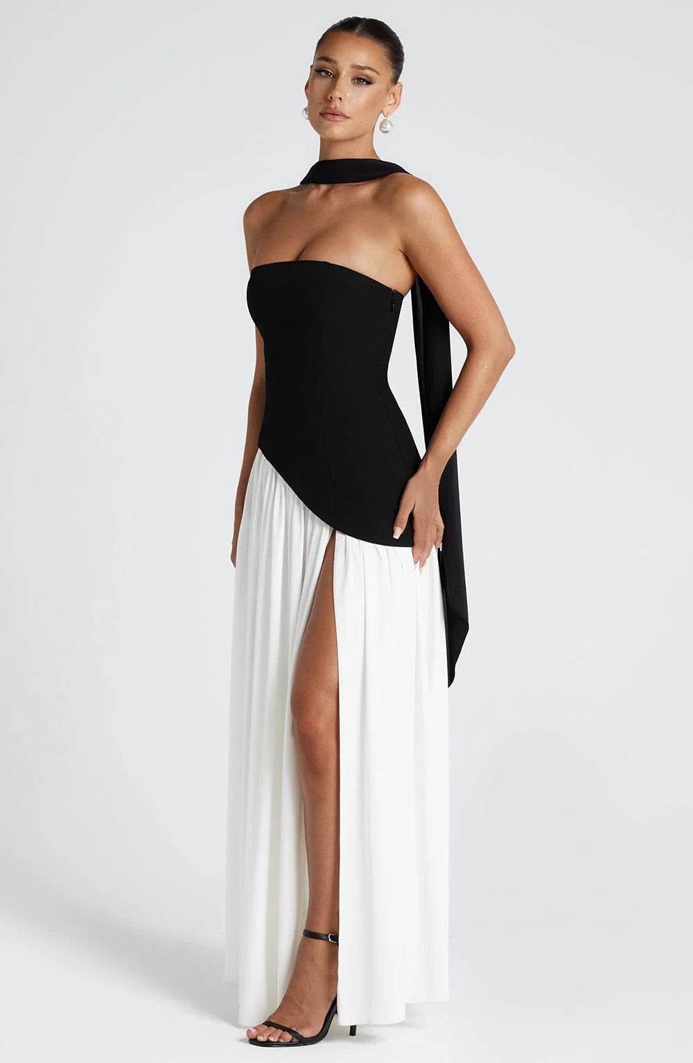 Side view of a black and white strapless asymmetric corset maxi dress, showcasing the high slit and flowing skirt.